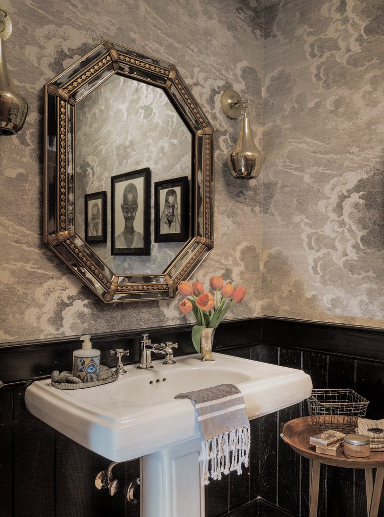 Powder room designed by Noelle Schoop Design, with cloud-pattern wallpaper, a Venetian octagonal mirror, dark wainscoting, and a pedestal sink